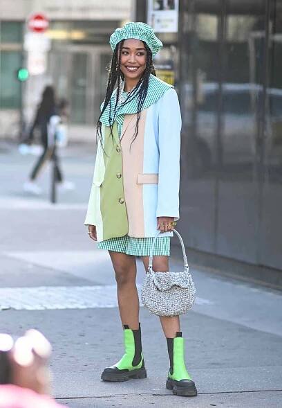 Woman wearing a gingham outfit with a colorful blazer overtop and green Chelsea boots.