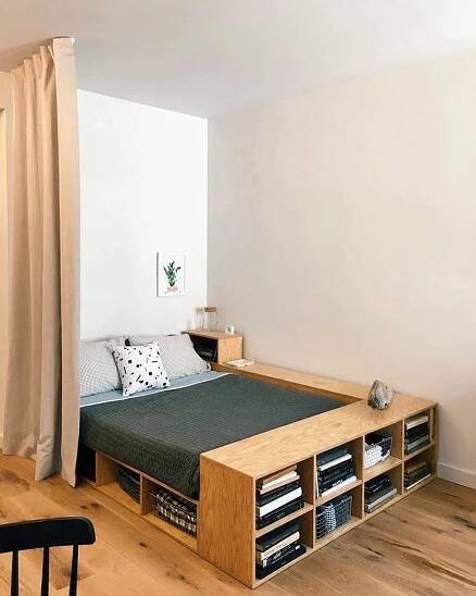 a bed sitting next to a window in a room with wooden floors and white walls