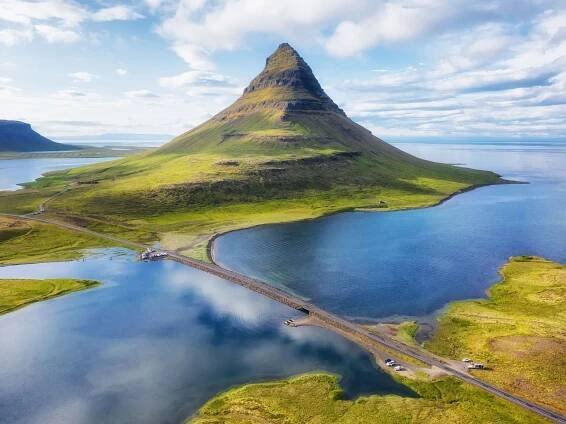 an aerial view of a mountain surrounded by a lake and a road .