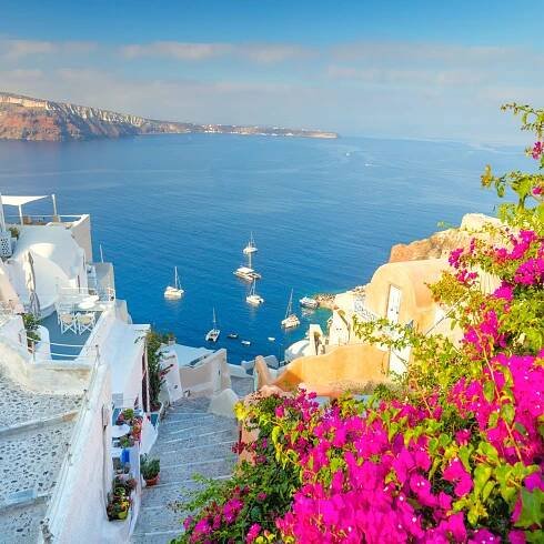 A narrow old street with flowers, traditional Greek houses and a staircase to the sea, Santorini island, Greece