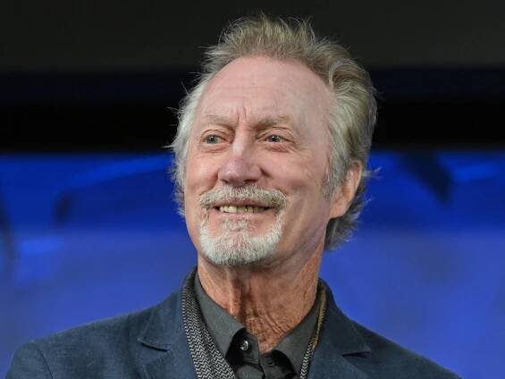 Bryan Brown smiles against a blue background.