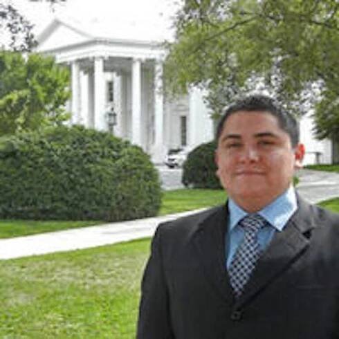 David Hernandez posing in front of a colonial styled building and shruberies.
