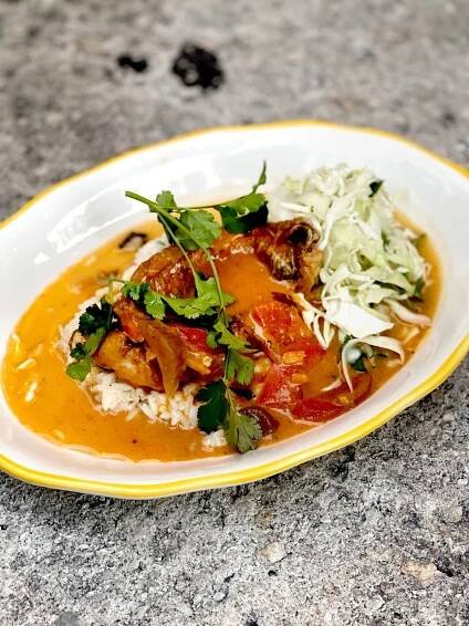 On a white plate with a thin yellow rim, a dish of yellowtail, rice and a golden sauce is garnished with herbs.