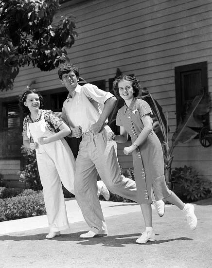 Buddy Ebsen, comic dancer, is never too busy to help a friend. Here he is showing Judy Garland and Deanna Durbin, MGM starlets, how to do a few of his famous dance steps. The young ladies are only thirteen.