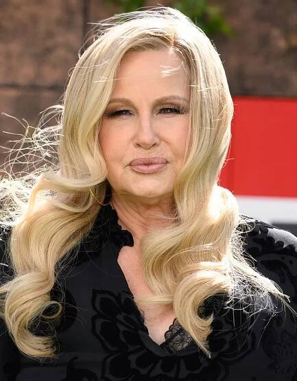 Person with long, wavy hair and elegant black attire outdoors, with a confident expression