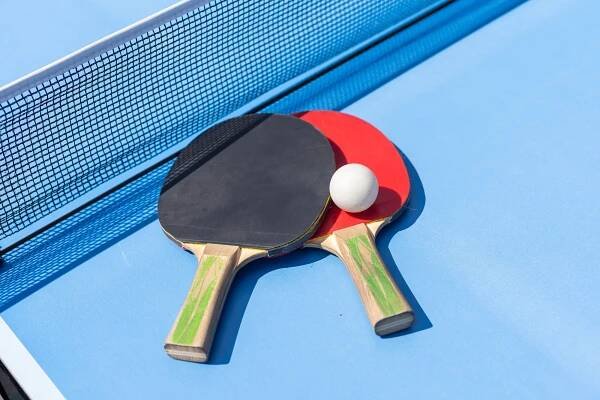 Two table tennis or ping pong rackets and ball on blue table with net
