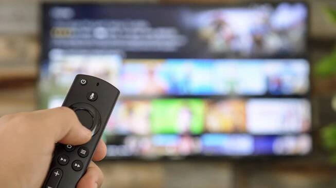 Mužská ruka drží dálkové ovládání a přepíná televizní kanály. Kanál surfování, zaměřený na ruku a dálkové ovládání. Internet TV. — Stock obrázek