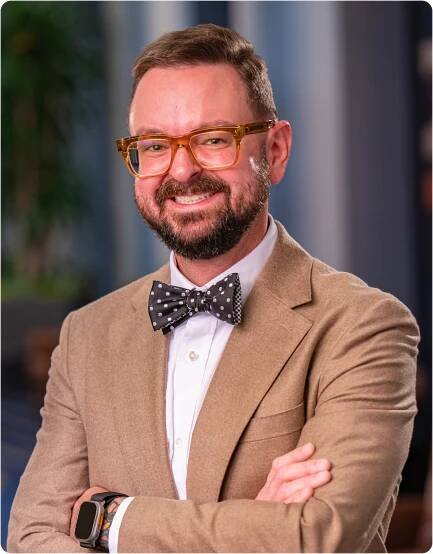 Headshot of Bradley in a khaki jacket and polka dot bowtie smiling at the camera