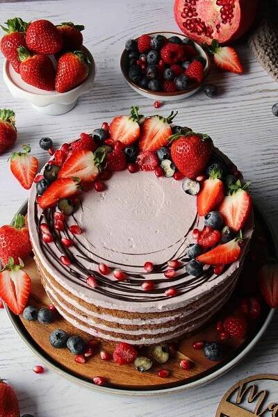 a cake with strawberries and blueberries is on a wooden platter surrounded by other desserts