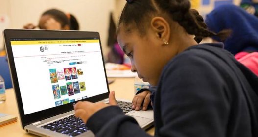 A young girl types on a laptop with an NYPL page on the screen