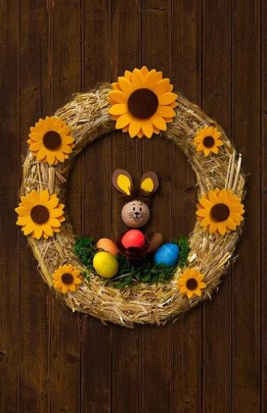 an easter wreath with sunflowers and a teddy bear in the center on a wooden wall