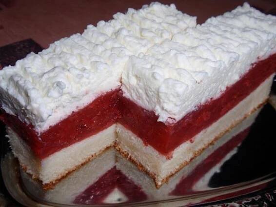 a layered cake with white and red frosting on a plate next to a fork