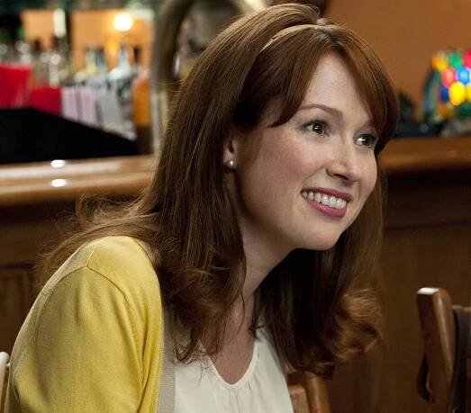 a woman sitting at a table in front of a bar smiling for the camera while wearing a yellow cardigan