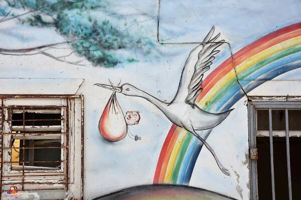 regenbogen davor storch mit baby in tuch