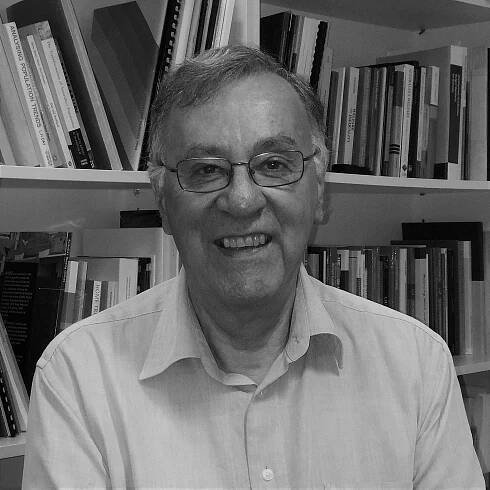A black and white profile picture of a person smiling, sitting in front of a bookcase.