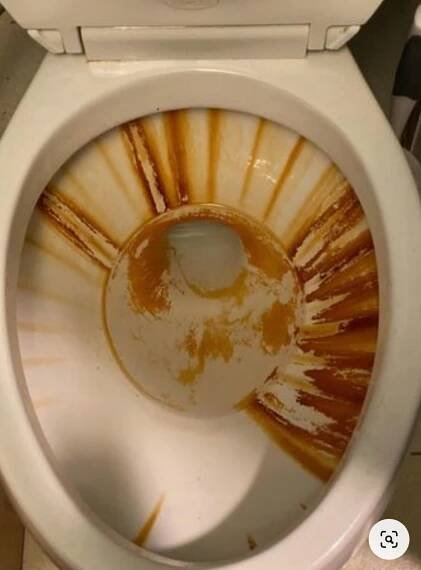 a white toilet with the lid up and some brown paint on it's rim