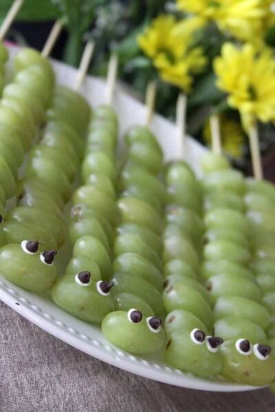 green grapes with googly eyes are arranged on a white plate next to yellow flowers