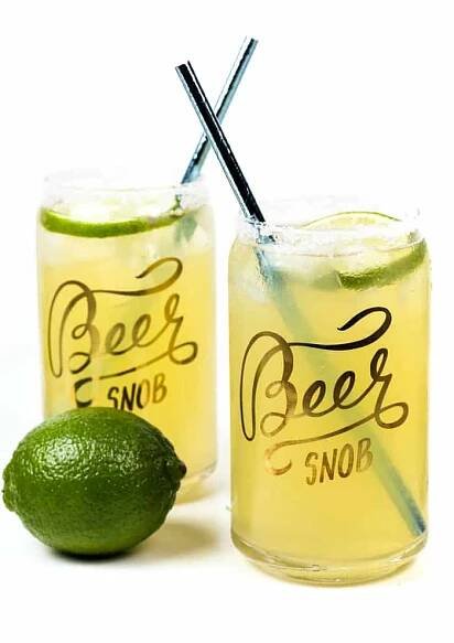 two beerita cocktails with blue straws and a fresh lime on a white background
