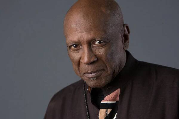 A portrait of Louis Gossett Jr., an older man with a shaved head wearing a brown jacket and a colorful tie.