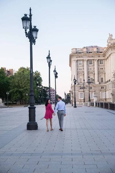 Two people walking hand in hand near Royal Palace of Madrid with ornate street lamps and classical architecture.