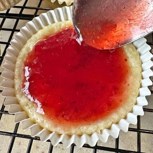 Spooning strawberry jam on a mini cheesecake.