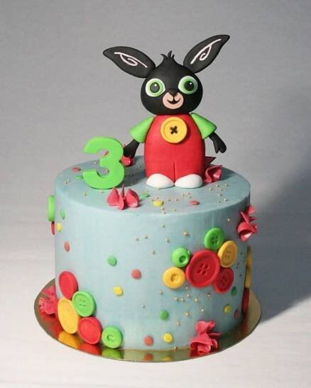 a birthday cake decorated with buttons and a bunny figure on top is shown in front of a white background