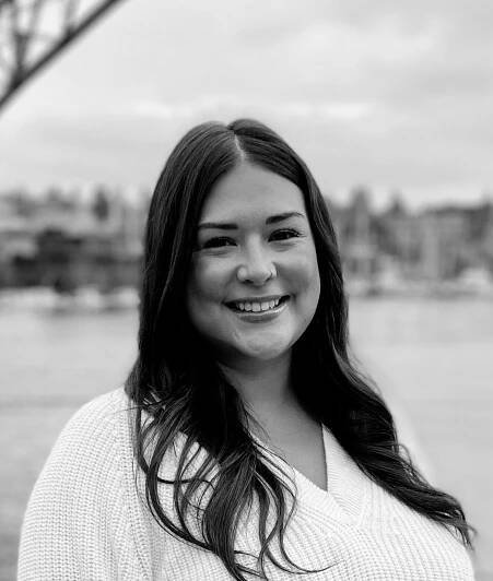 A woman in a white sweater is smiling in a black and white photo.