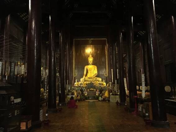 Photo of shining gold Buddha statue inside temple at sunset Wat Phan Tao in Chiang Mai, Thailand