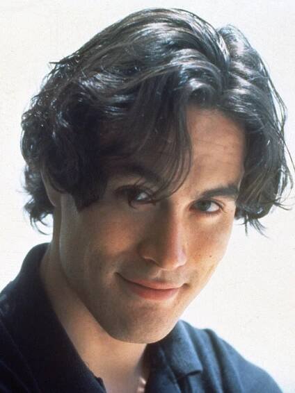 a close up of a person wearing a black shirt and looking at the camera with a smile on his face