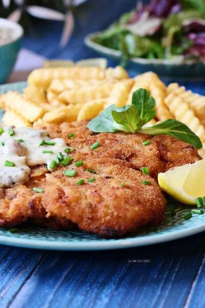 Chicken schnitzel with fries and a salad on the back.