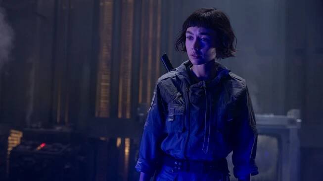 A woman stands in a blue-lit room.
