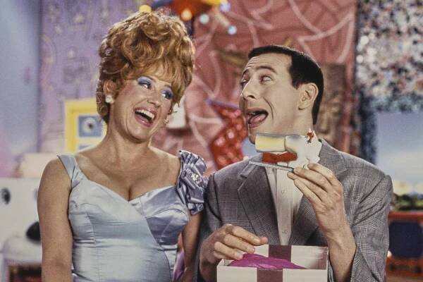 Lynne Marie Stewart, wearing a blue dress, beside American actor and comedian Paul Reubens, who wears his trademark glen plaid suit over a white shirt and red bow tie, holding an ornament shaped like the hind quarters of a dog, in CBS children's television series 'Pee-wee's Playhouse'