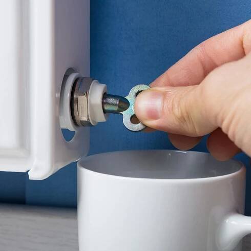 Jemand entlüftet einen Heizkörper mit einem Entlüftungsschlüssel. Darunter eine Tasse zum Auffangen des Wassers.