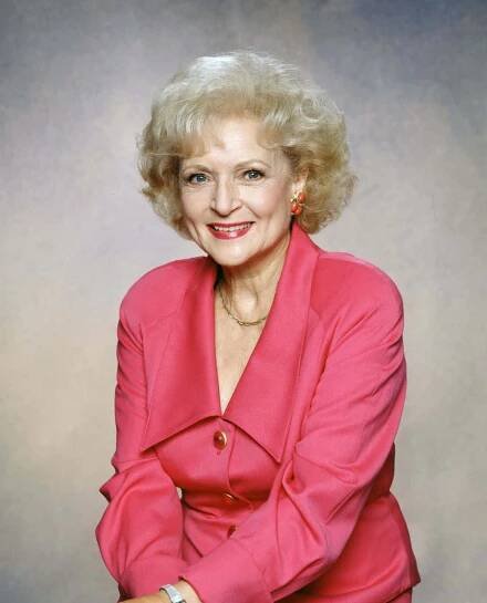 an older woman in a pink suit posing for a studio portrait with her hands on her knees