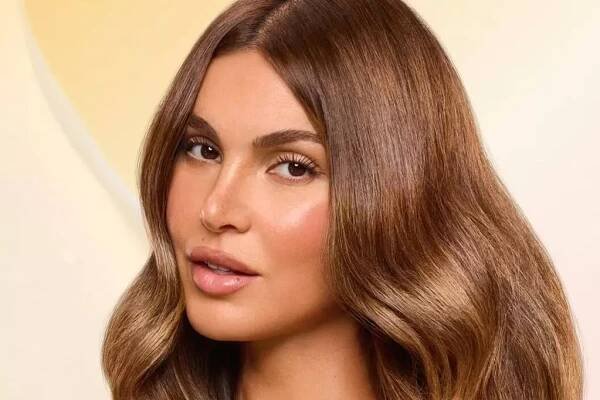 Model with long brown glossy hair holds gisou hair mask in yellow pot