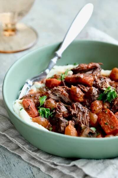 Short Ribs Bourguignon over mashed potatoes in sage green bowl with fork.