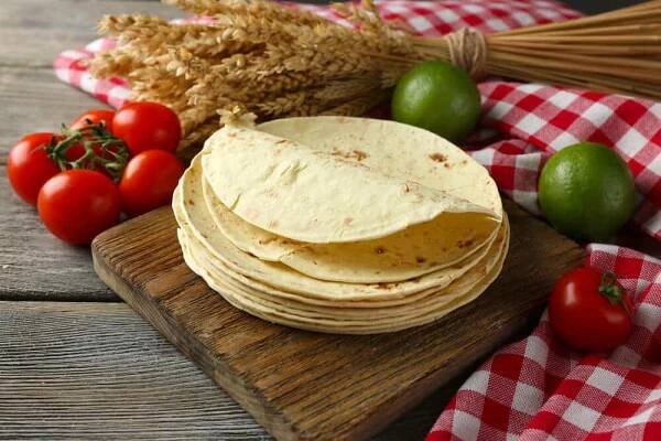 Zásobníku celozrnný domácí moučná tortilla a zeleniny na prkénko, na dřevěný stůl pozadí — Stock obrázek