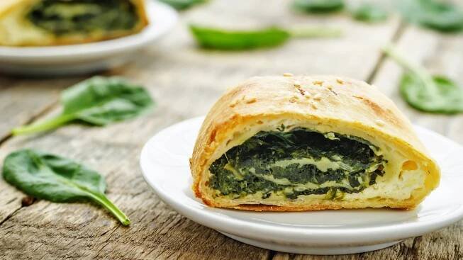 Spinatstrudel mit Ricotta / angeschnitten / frische Spinatblätter / Untergrund Holz / Frontal