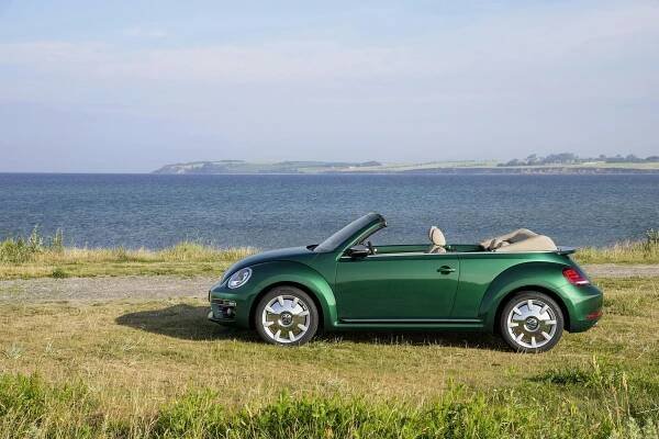 Grünes Cabrio parkt am Meer auf einem Grasfeld, bei klarem Himmel und ruhiger See im Hintergrund.