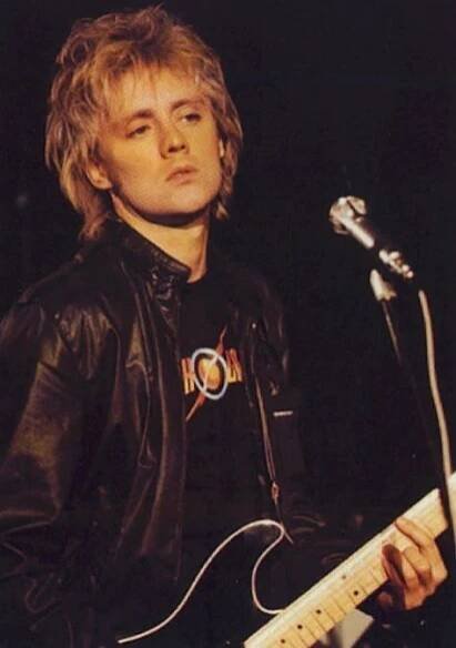 a man with blonde hair playing an electric guitar in front of a microphone on stage