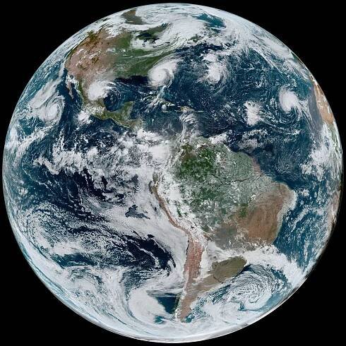 GOES-16 image of Earth showing four tropical storms in white, blue, green and orange colors.