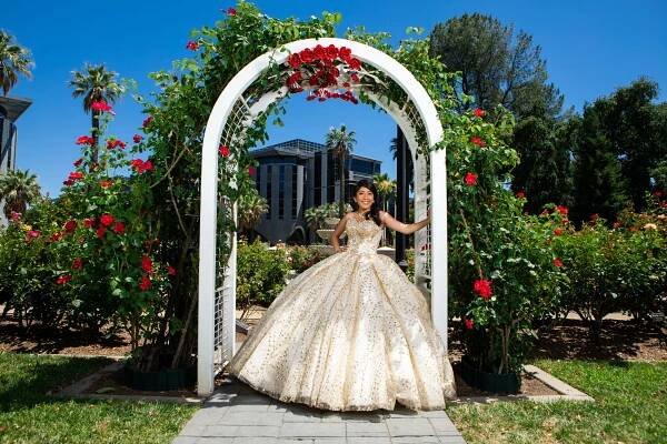 Ornate white garden arch with red roses framing a formal dress celebration photo.