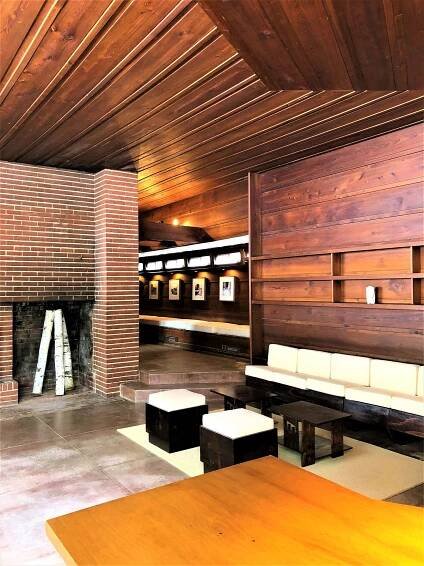 A brick fireplace with aspen logs in it stands across from a built-in couch and wood walls.