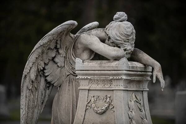 Cemetery statue of an angel with head bent over the headstone. Rochester, NY