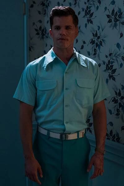 a man in a blue shirt and green pants standing next to a wall with flowers on it