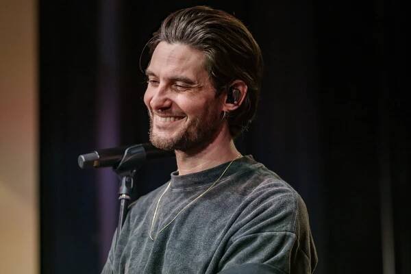 Man smiling while wearing casual sweater, standing near a microphone
