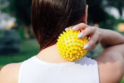 Zblízka na zádech mladé ženy, která provádí masáž šíje a ramen s ostnatým gumovým míčkem, uvolňuje napjaté krční svaly — Stock obrázek