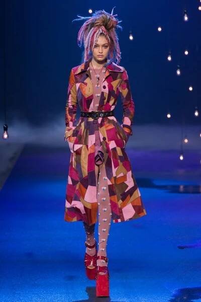 a model walks down the runway in a multicolored coat and matching red boots