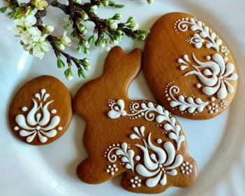 three decorated cookies sitting on top of a white plate next to a branch with flowers