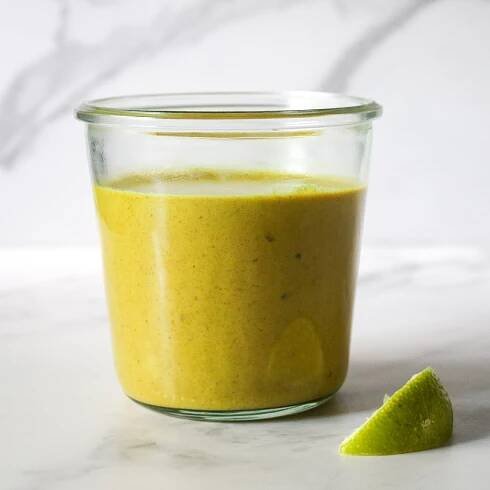 A glass jar filled with coconut curry sauce next to a slice of lime.